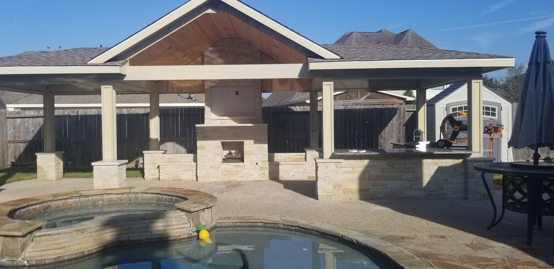 Backyard patio with covered grill area, pool in front, and mountains in the background.