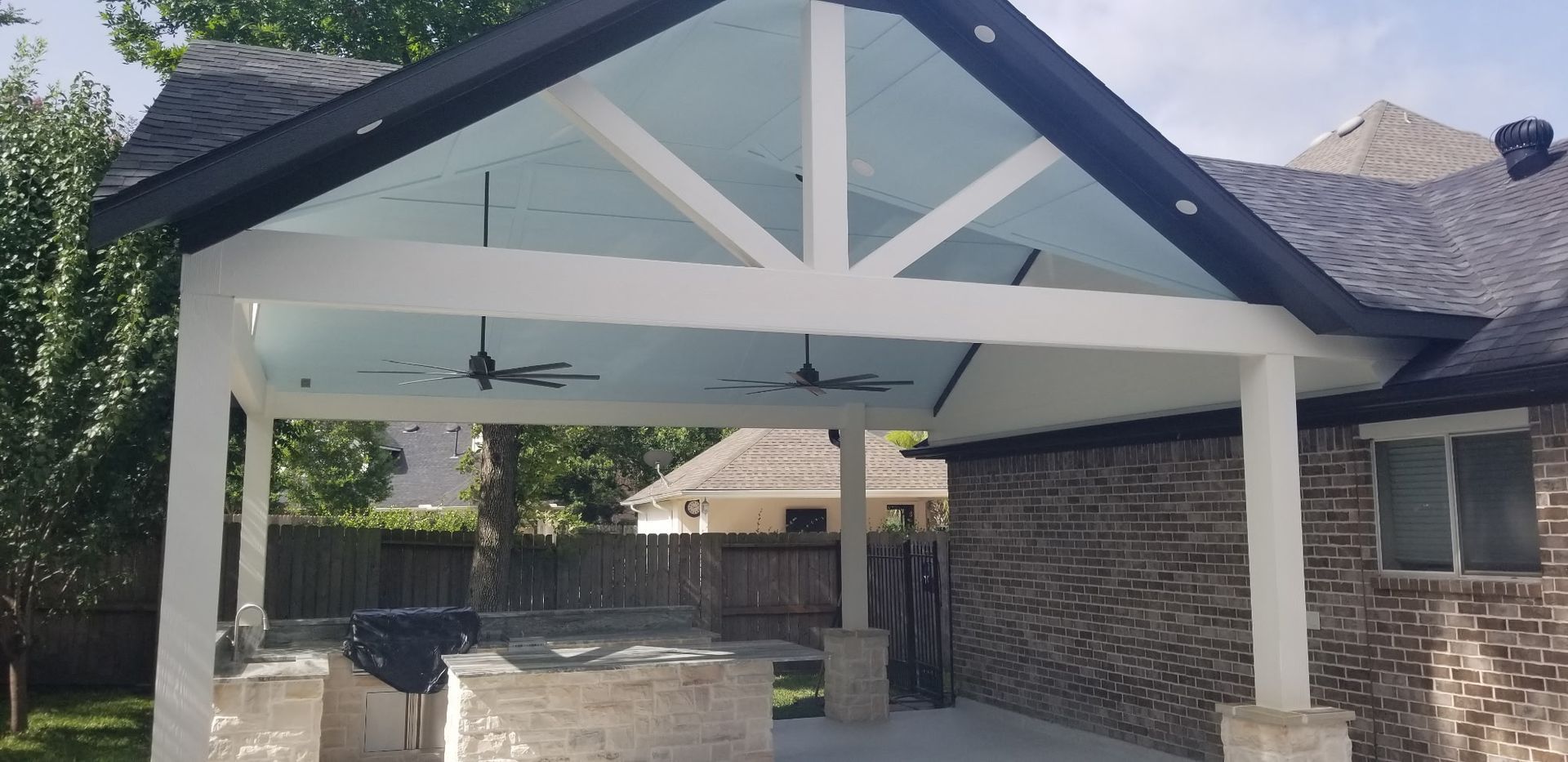 Covered outdoor entrance with white beams, dark roof trim, stone pillars, and shaded seating area