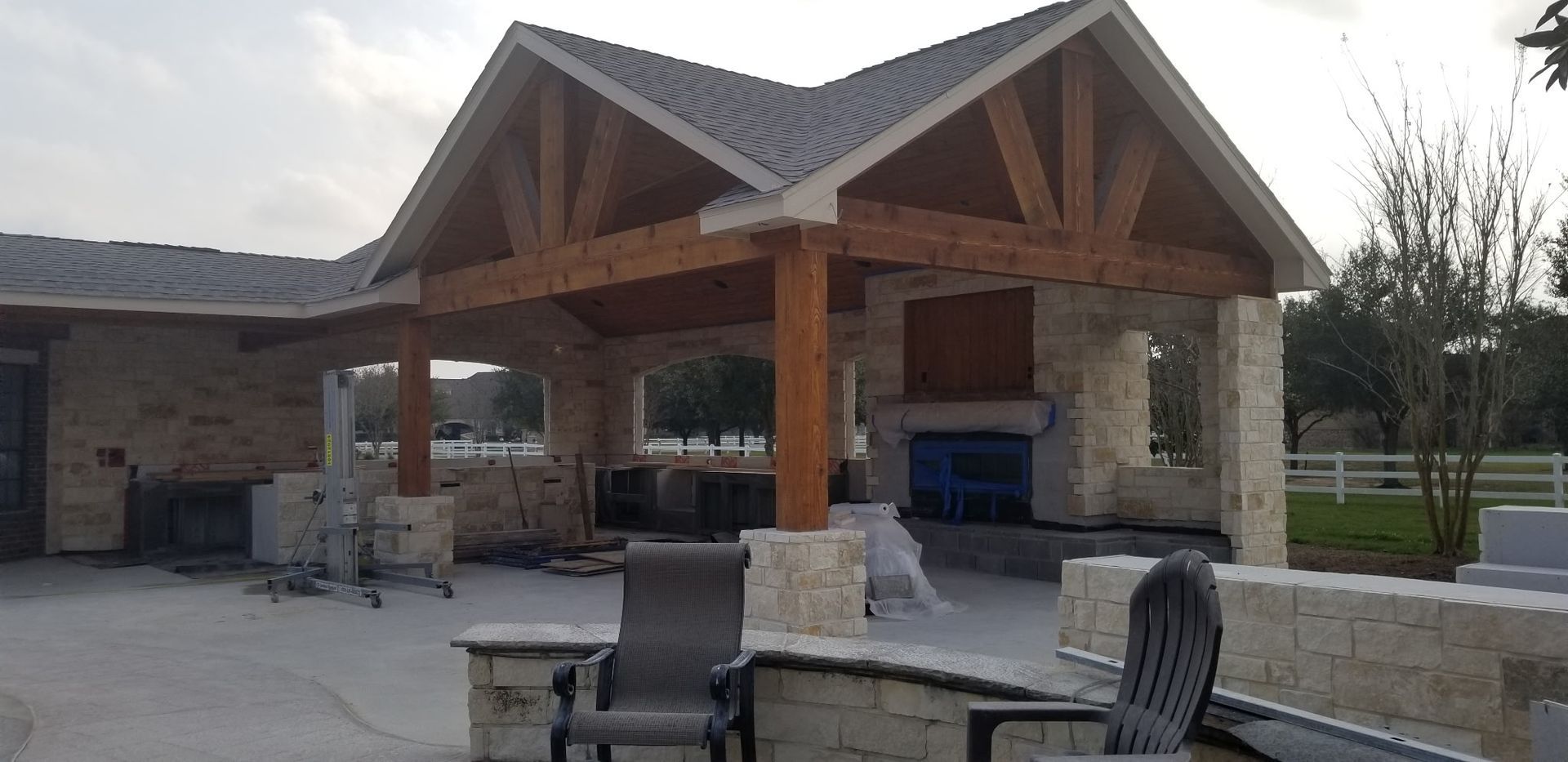 Outdoor pavilion with wooden roof, stone columns, and patio seating at a park