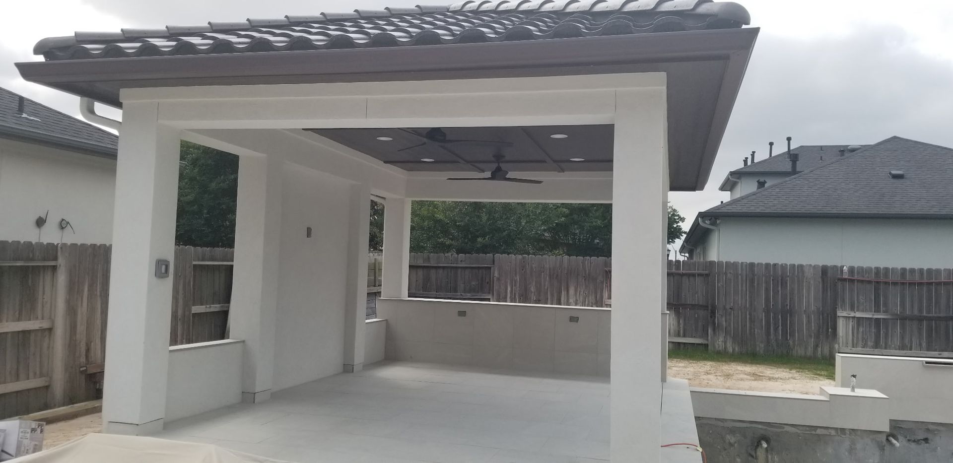 Covered backyard patio with white columns, concrete floor, and a fenced yard behind it.