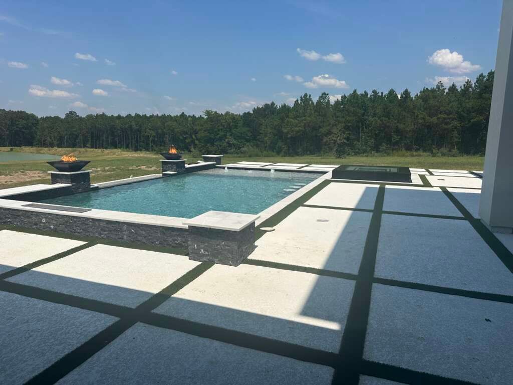 Modern outdoor pool with blue water, white tile deck, and trees under a clear sky