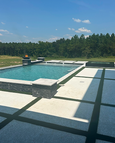 Modern backyard pool with turquoise water, white patio, and green trees under a clear blue sky