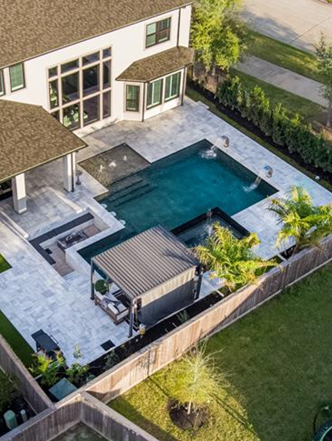 Aerial view of a modern backyard with a rectangular pool, patio, and pergola beside a house.