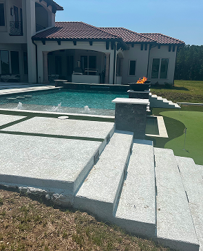 Stone steps leading to a backyard pool and modern house with a lit fire feature on the patio