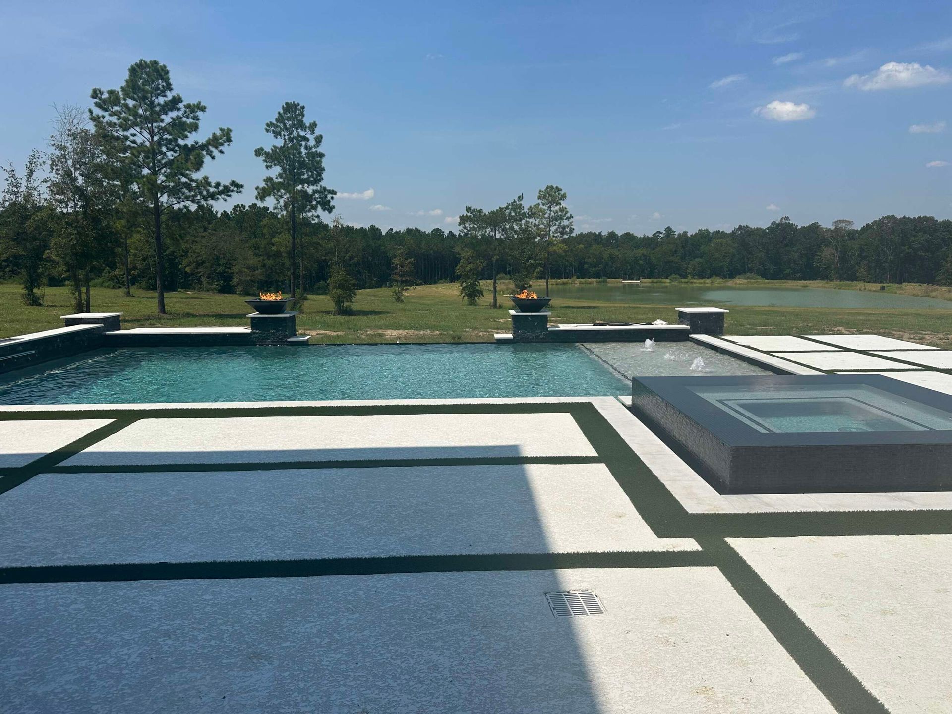 Patio with pool and spa overlooking a grassy landscape and trees under a clear blue sky
