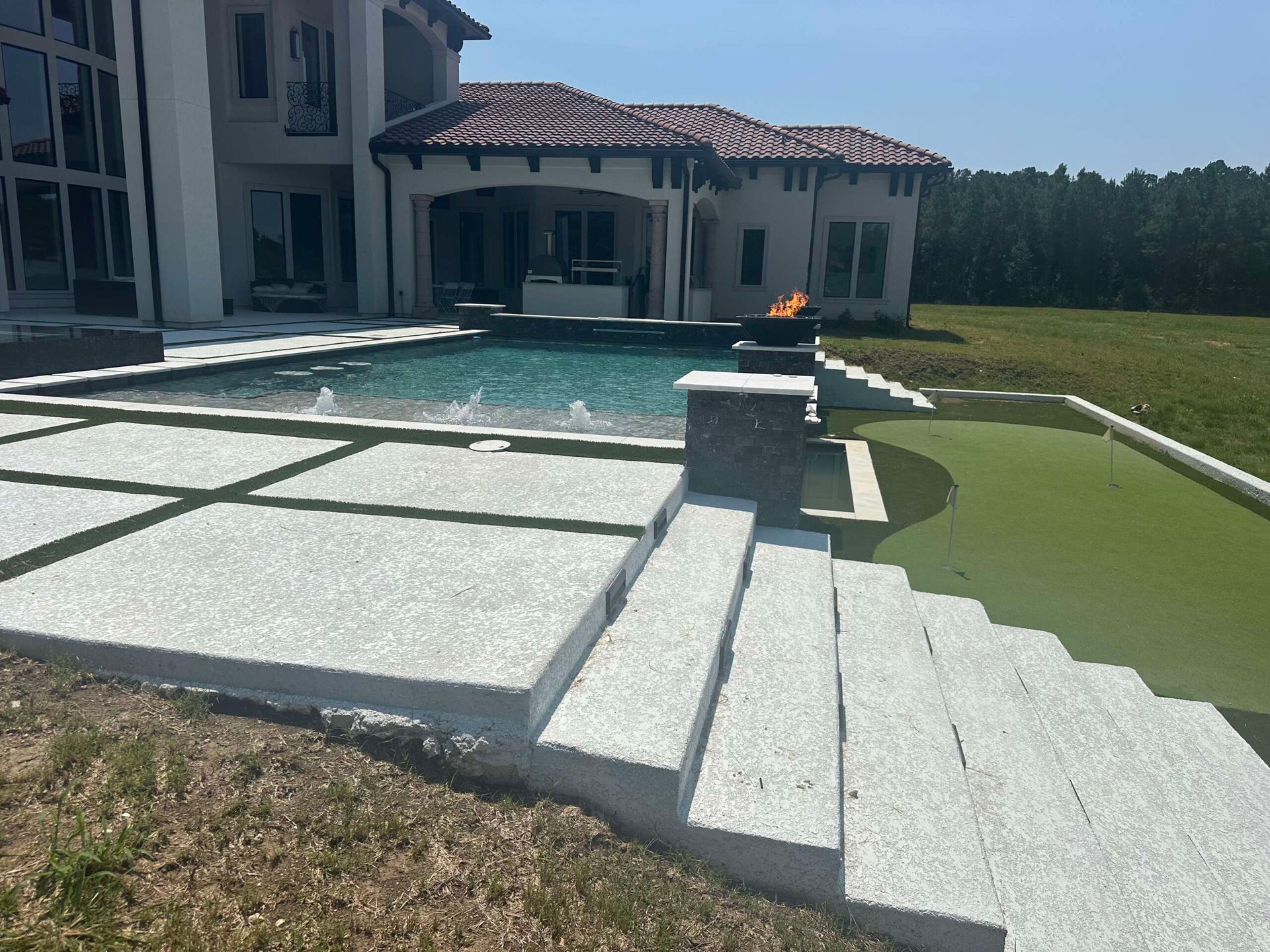 Backyard pool with stone patio, steps, and a white house with red-tile roof