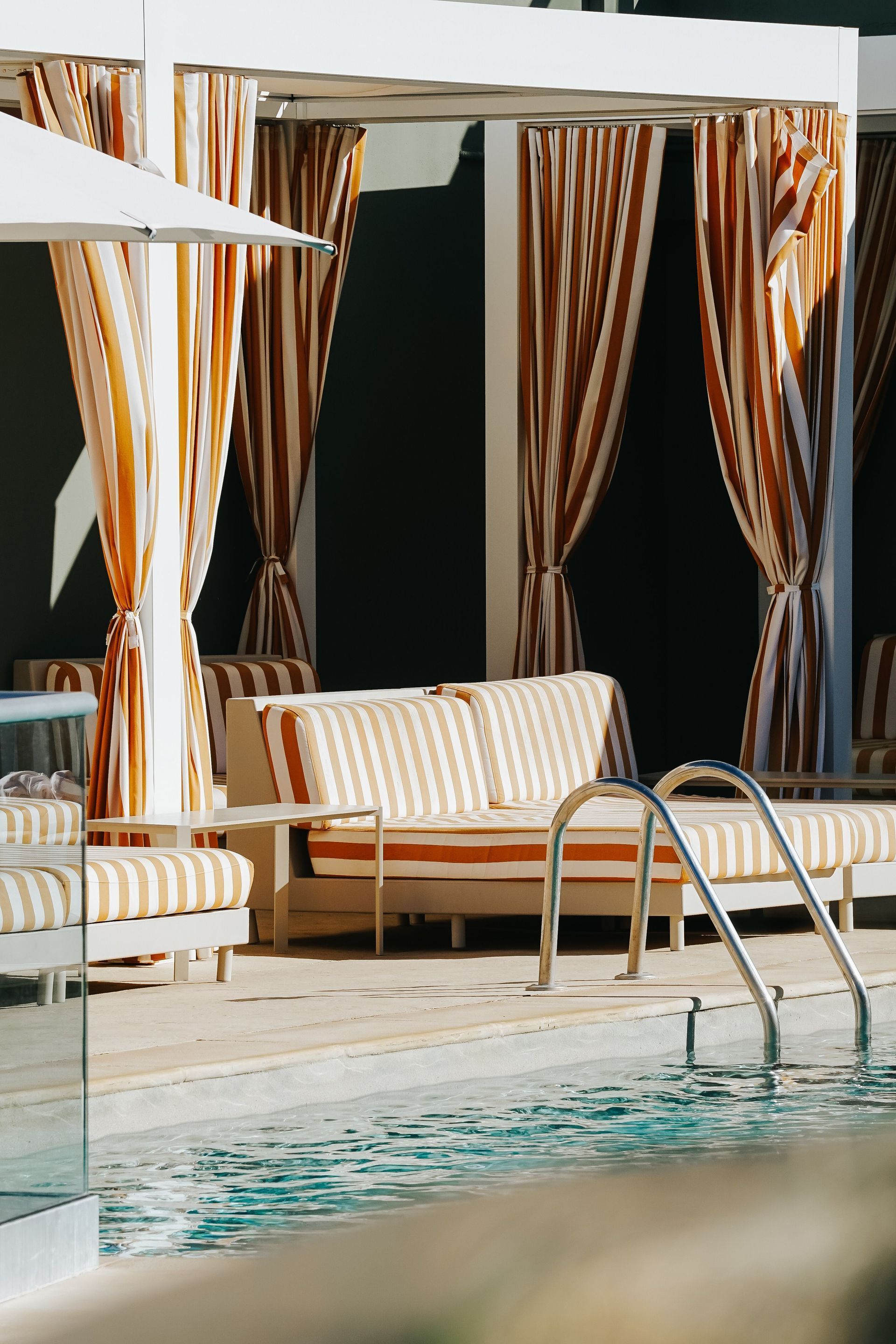 Luxury poolside cabana with palm trees and ocean view under a clear blue sky