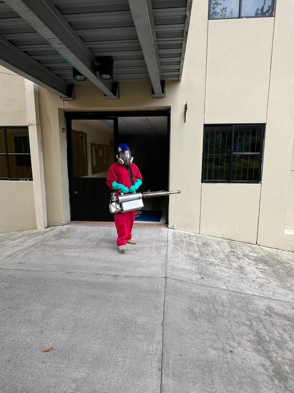 Persona con traje de materiales peligrosos desinfectando una entrada con un rociador.