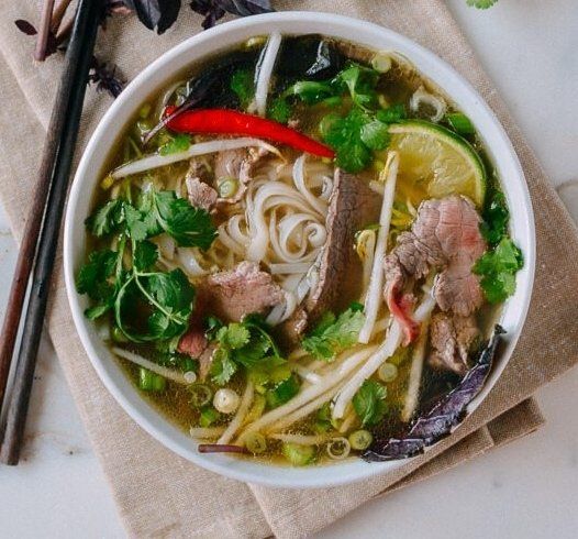 A bowl of soup with noodles , meat , vegetables and chopsticks on a table.