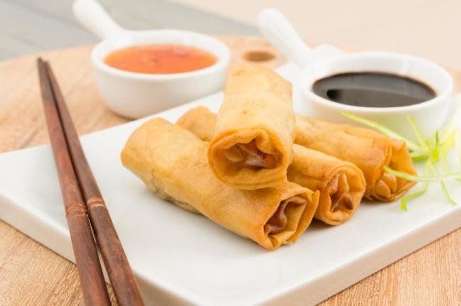 A plate of spring rolls with dipping sauce and chopsticks on a table.