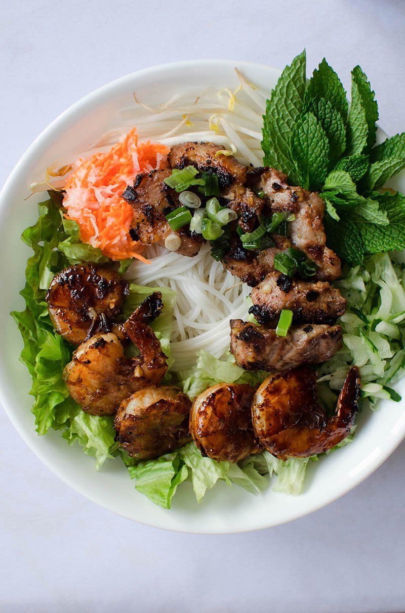 A white bowl filled with noodles , shrimp , meat and vegetables.