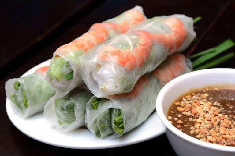 A plate of shrimp spring rolls next to a bowl of dipping sauce