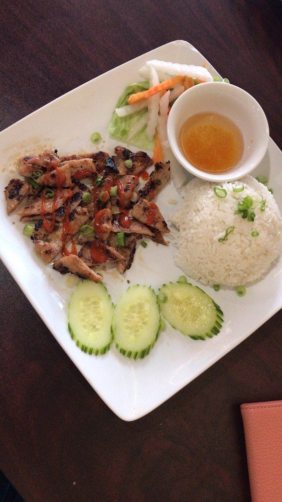 A plate of food with rice , meat , cucumbers and vegetables on a table.