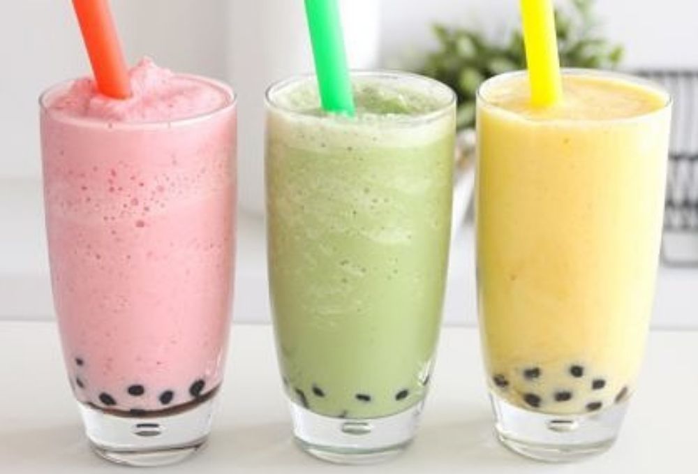 Three smoothies with straws in them are sitting on a table.