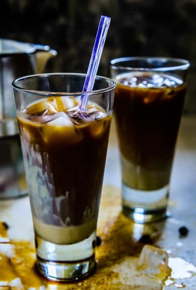 Two glasses of iced coffee with straws on a table.