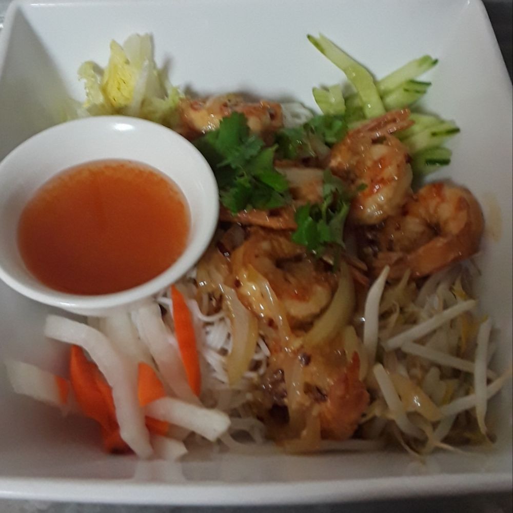 A bowl of food with shrimp and noodles and a small bowl of sauce