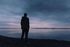 A man is standing on the shore of a lake looking at the water.