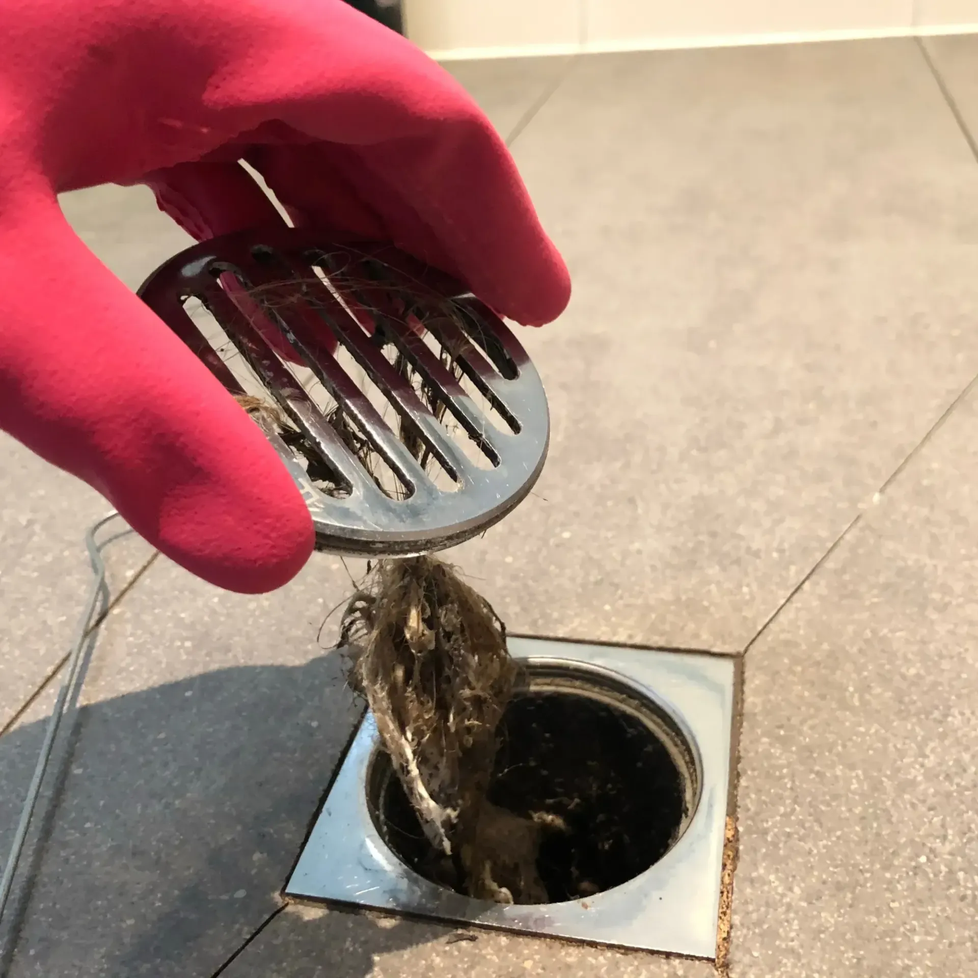 B&B Plumbing - A person wearing a pink glove is cleaning a drain