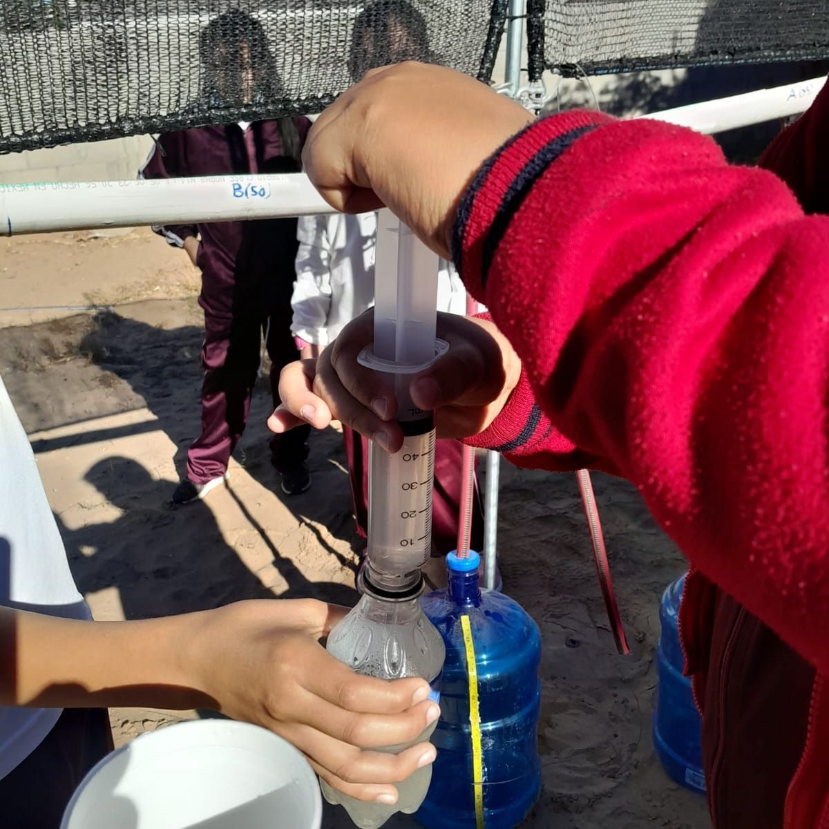 A person in a red sweatshirt is holding a syringe and a bottle of water