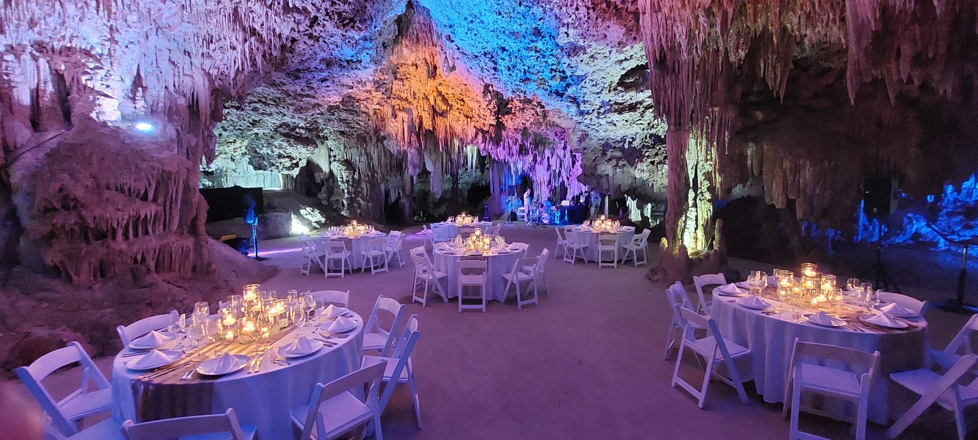 A group of tables and chairs in a cave with candles on them.