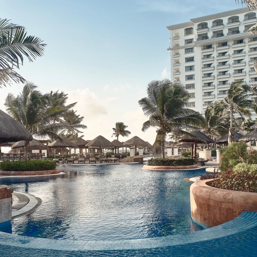 A large swimming pool surrounded by palm trees and a building