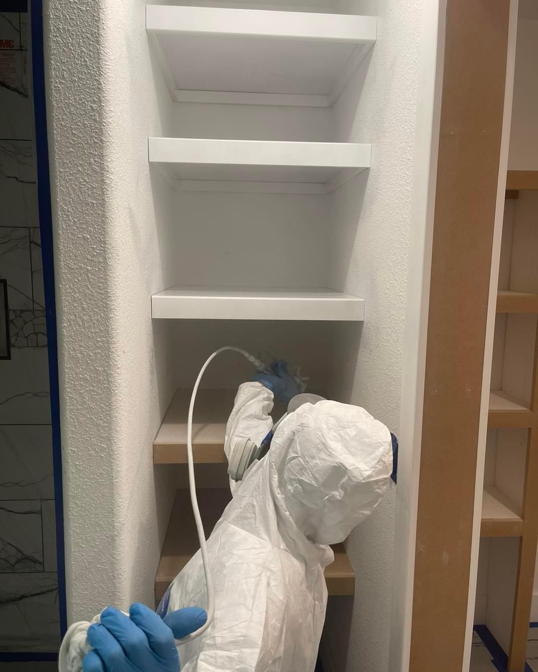 A person in a protective suit is spraying something in a closet.