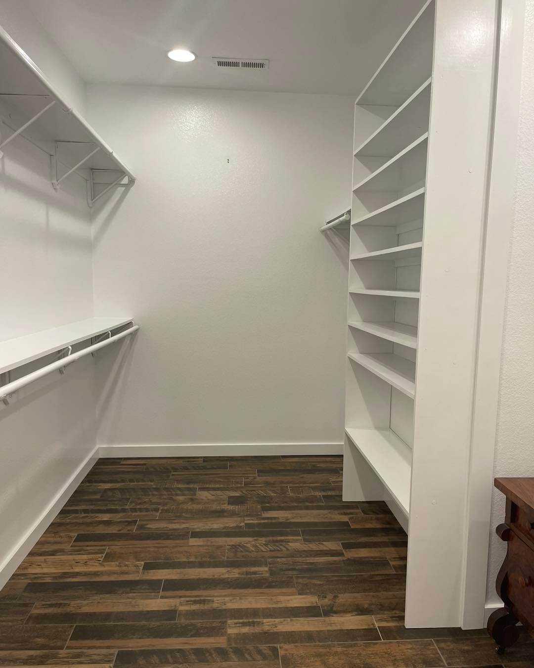 A walk in closet with wooden floors and white shelves.