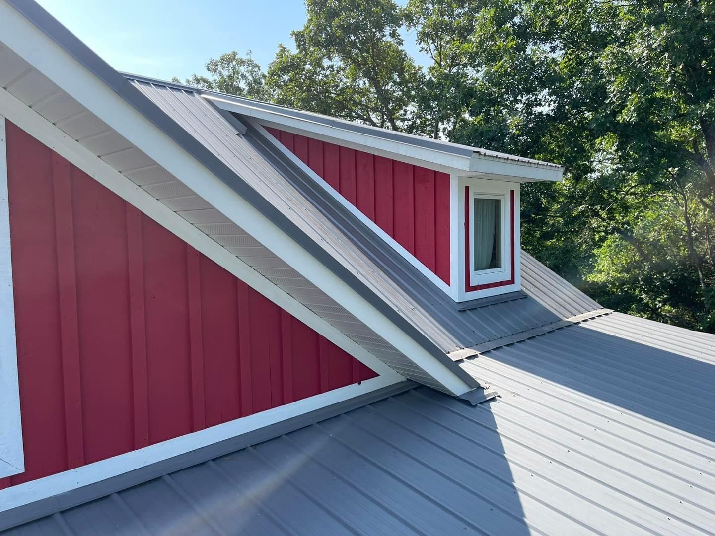 A red house with a gray roof and a window on the roof.