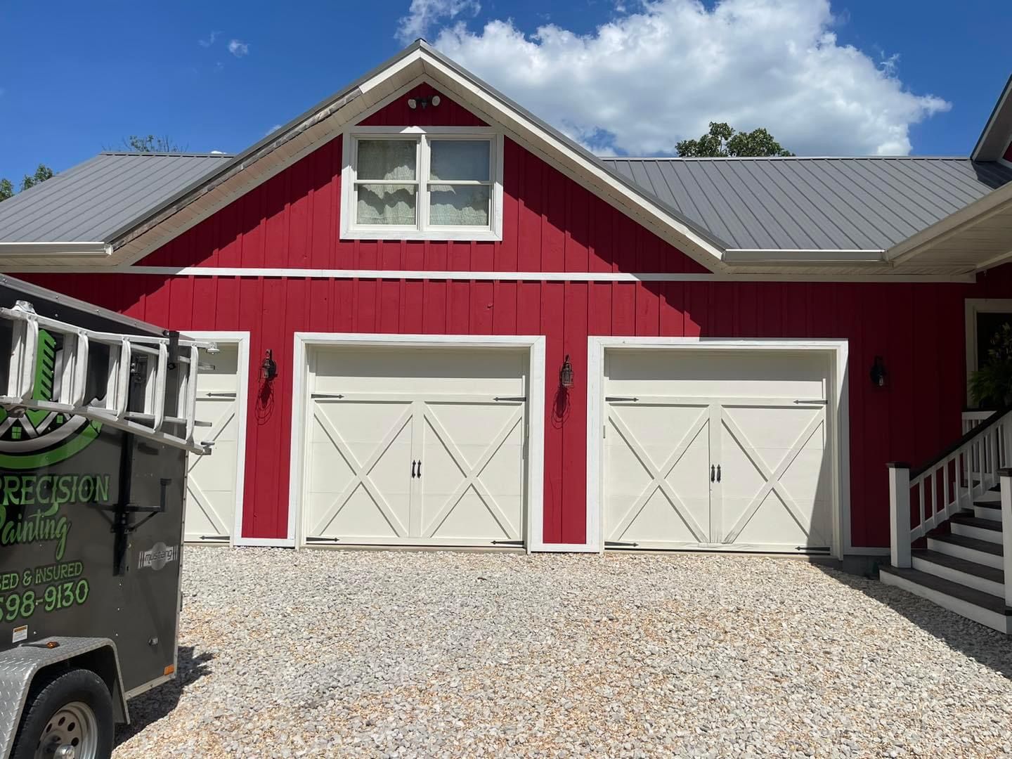A red house with white garage doors and a trailer parked in front of it.