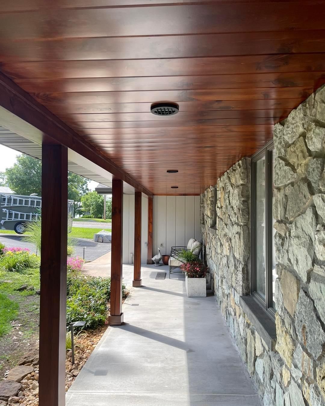 A porch with a wooden ceiling and a stone wall.