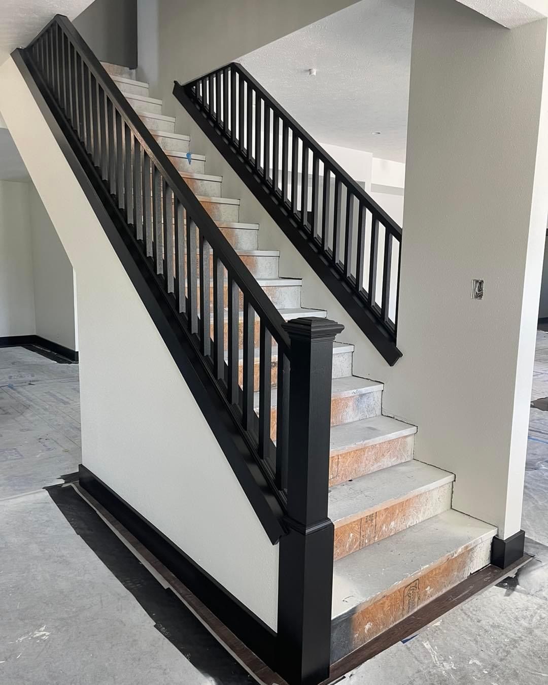 A staircase with a black railing is in a room with white walls.