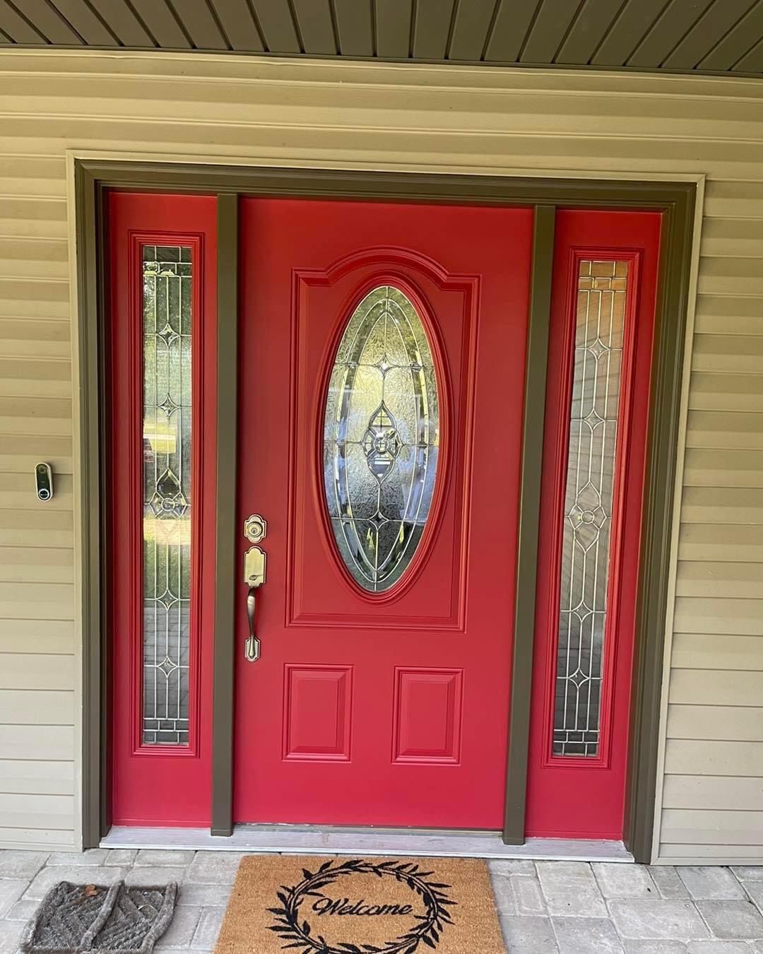 A red door with a stained glass window is on the front of a house.