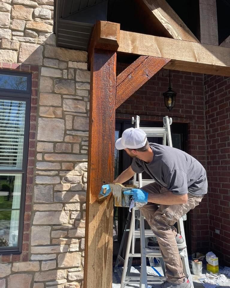 A man is standing on a ladder painting a wooden post.