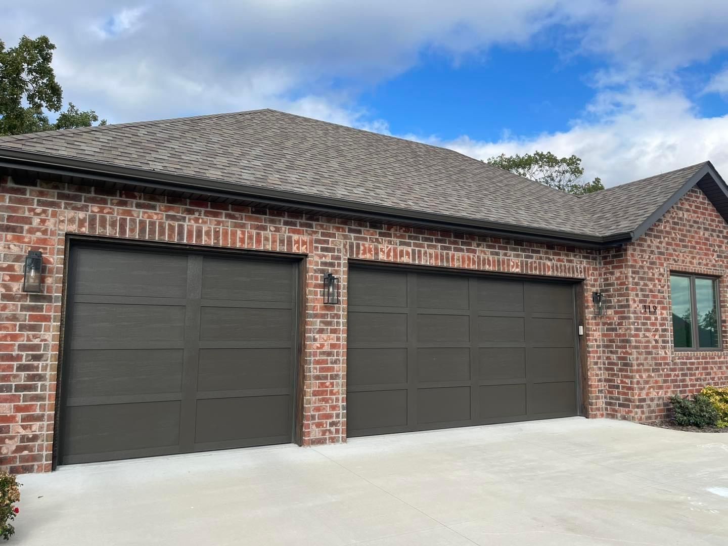 A brick house with three garage doors and a gray roof.