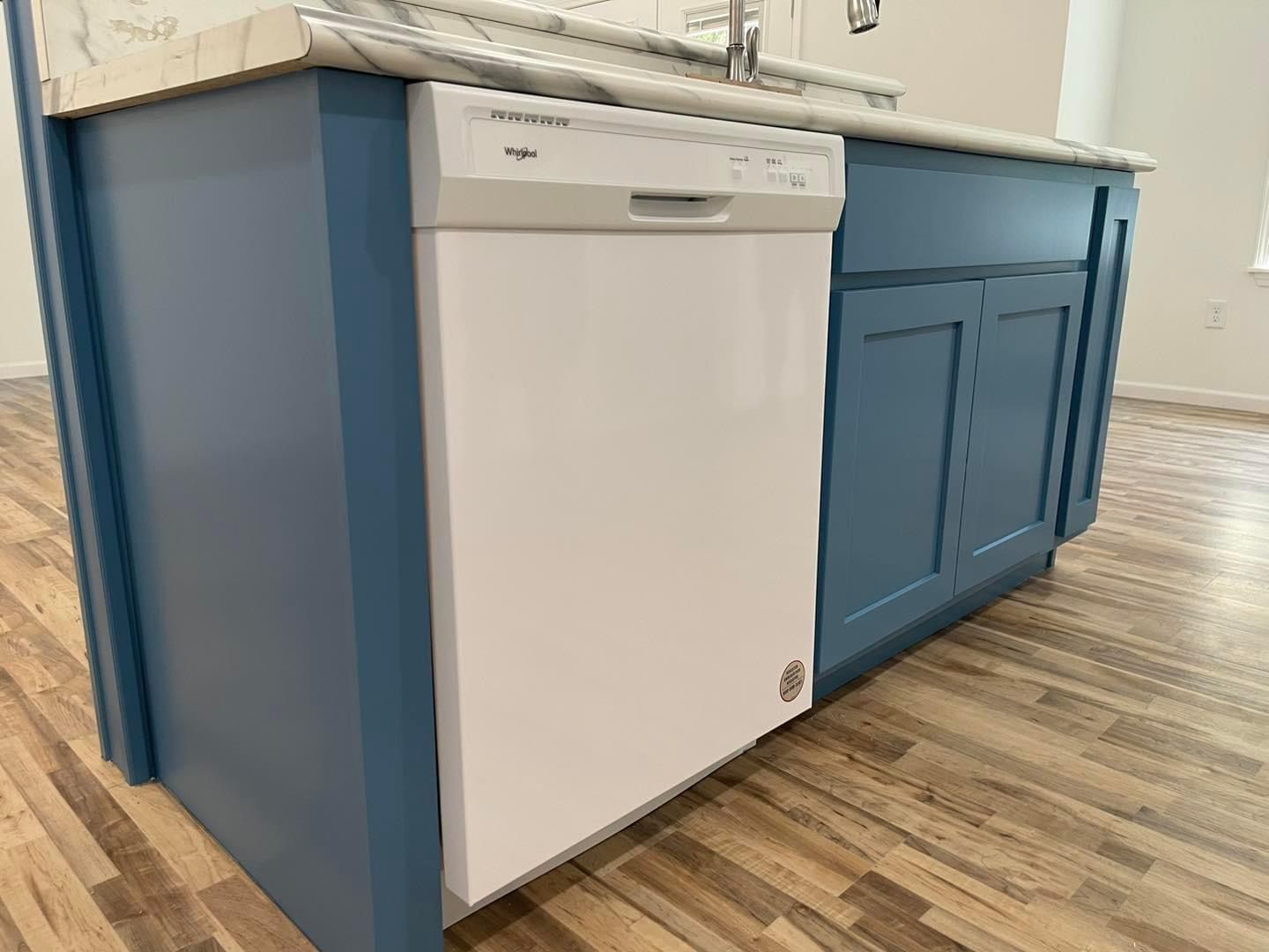 A white dishwasher is sitting under a blue cabinet in a kitchen.
