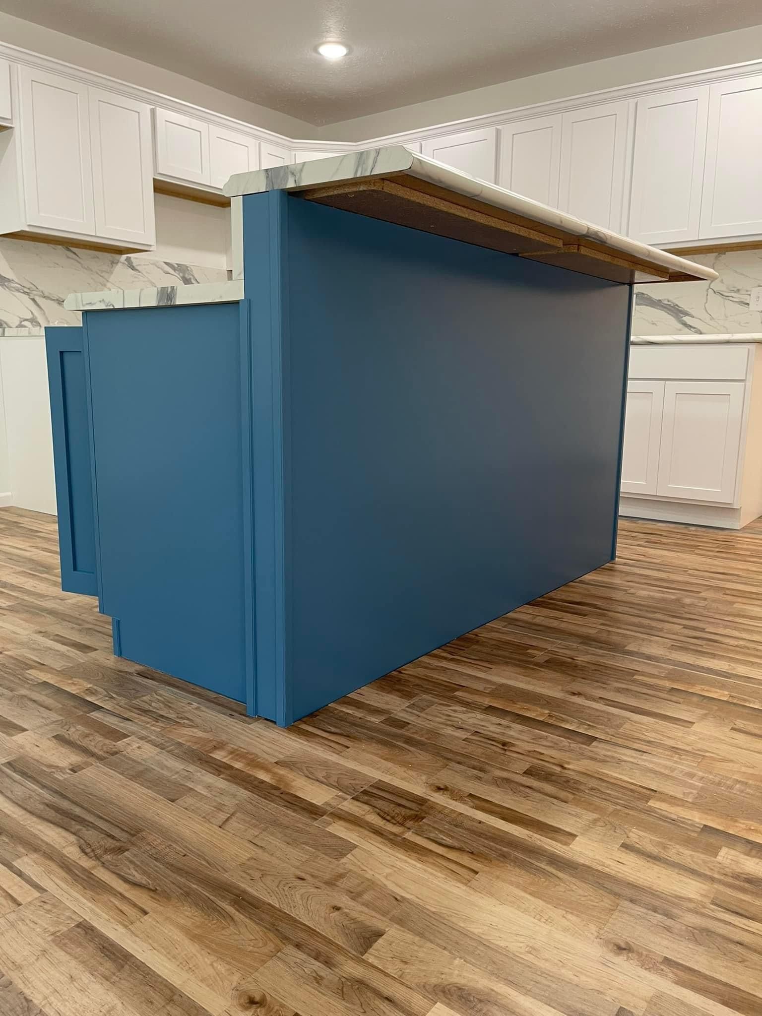 A blue island in a kitchen with white cabinets and hardwood floors.