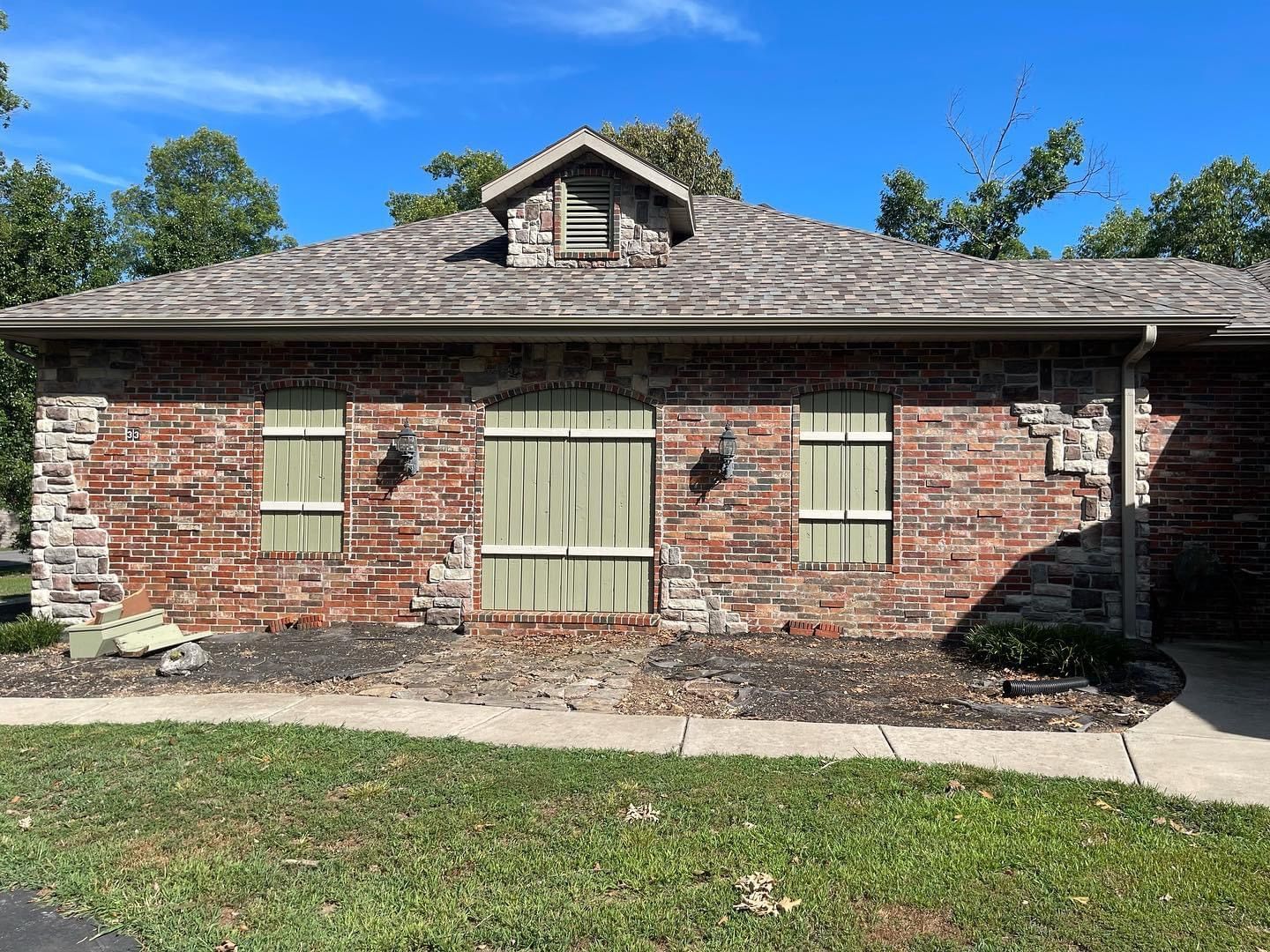 A brick house with green shutters on the windows and a roof.