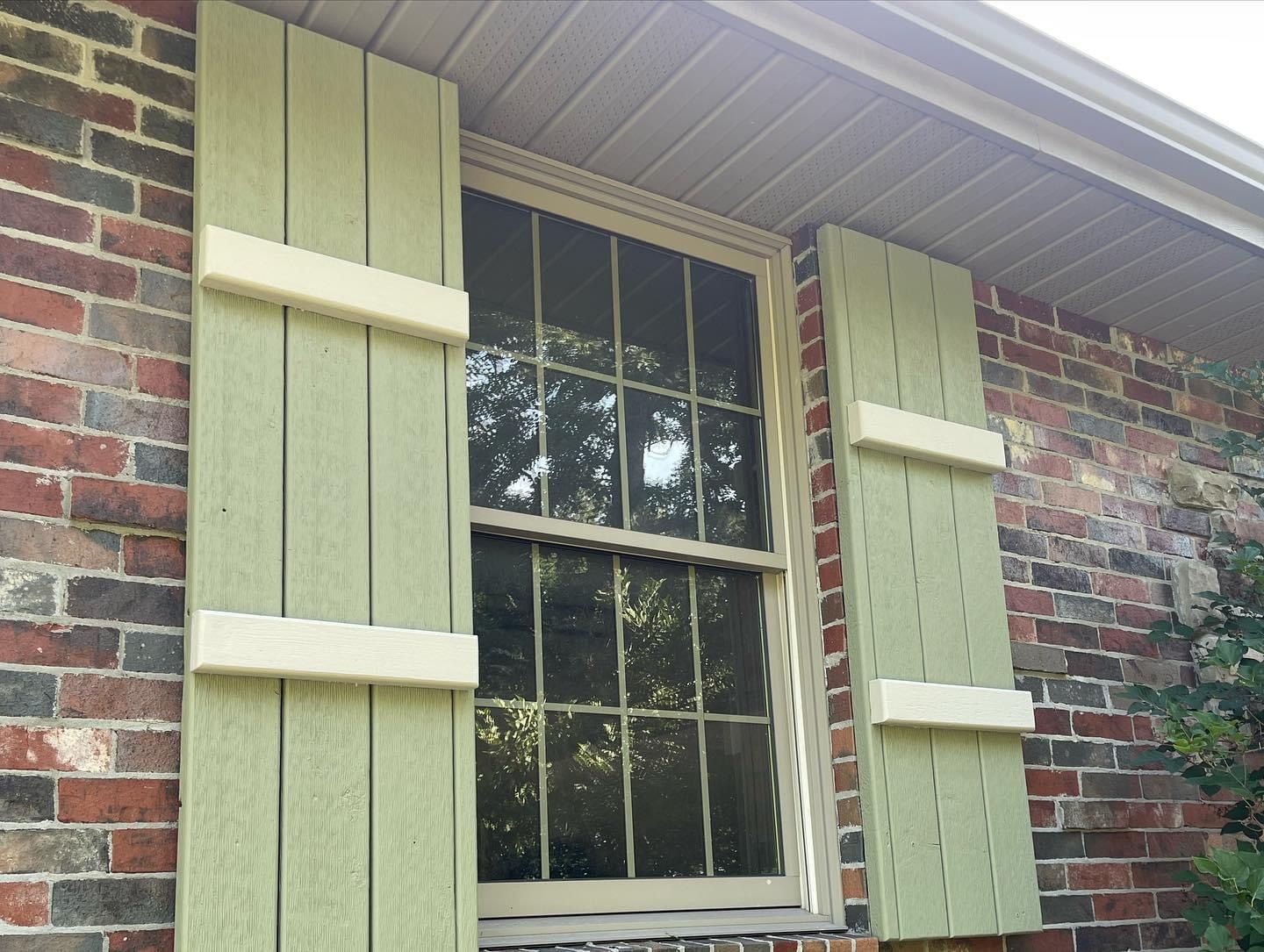 A window with green shutters on a brick building