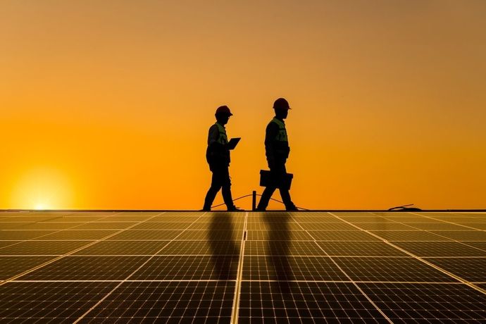 Two Men Are Walking on a Solar Panel at Sunset — B2B Electrical and Solar In Currimundi, QLD Two Men Are Walking on a Solar Panel at Sunset — B2B Electrical and Solar In Currimundi, QLD