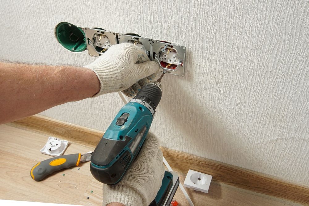 A Man Is Using a Drill to Install a Socket on A Wall — B2B Electrical and Solar In Caloundra, QLD