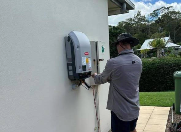 A Man Is Installing a Solar Panel on The Side of A Building — B2B Electrical and Solar In Currimundi, QLD