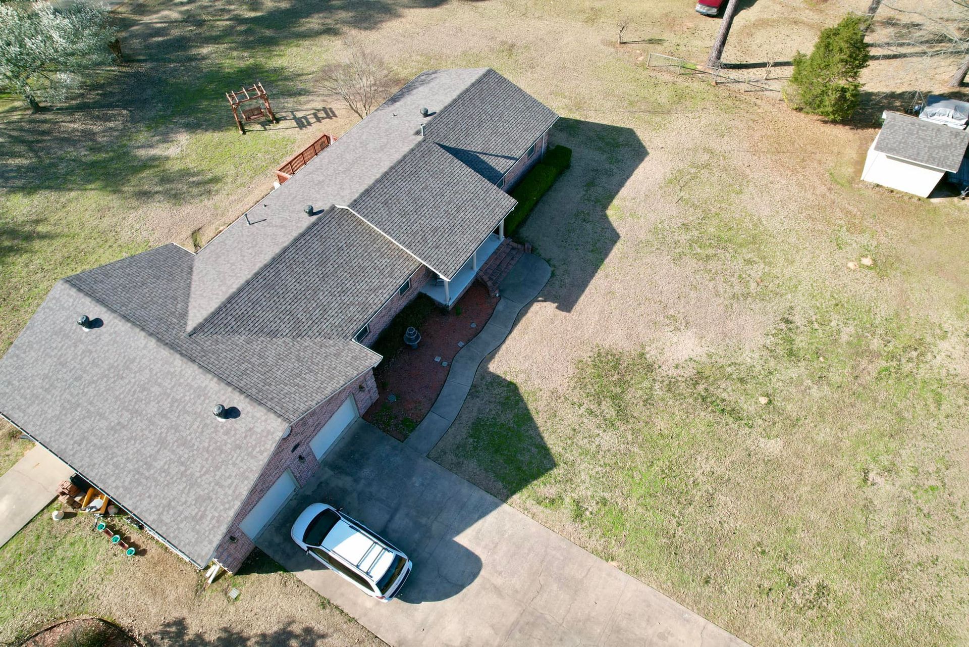 Overhead view of a house with a gray roof, brick exterior, driveway, and parked car on a grassy lot.
