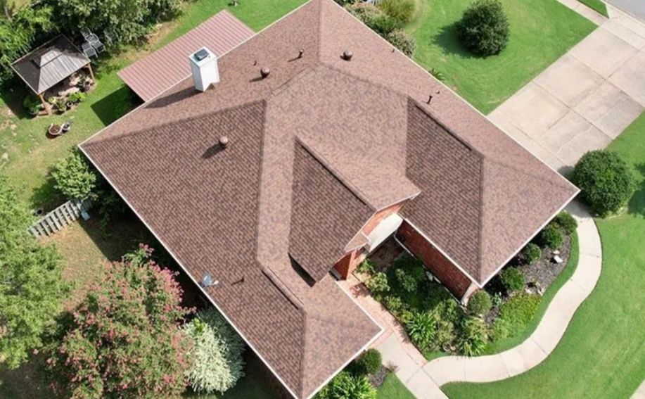 Brown shingle roof on a house with a concrete driveway and green lawn. Aerial view.