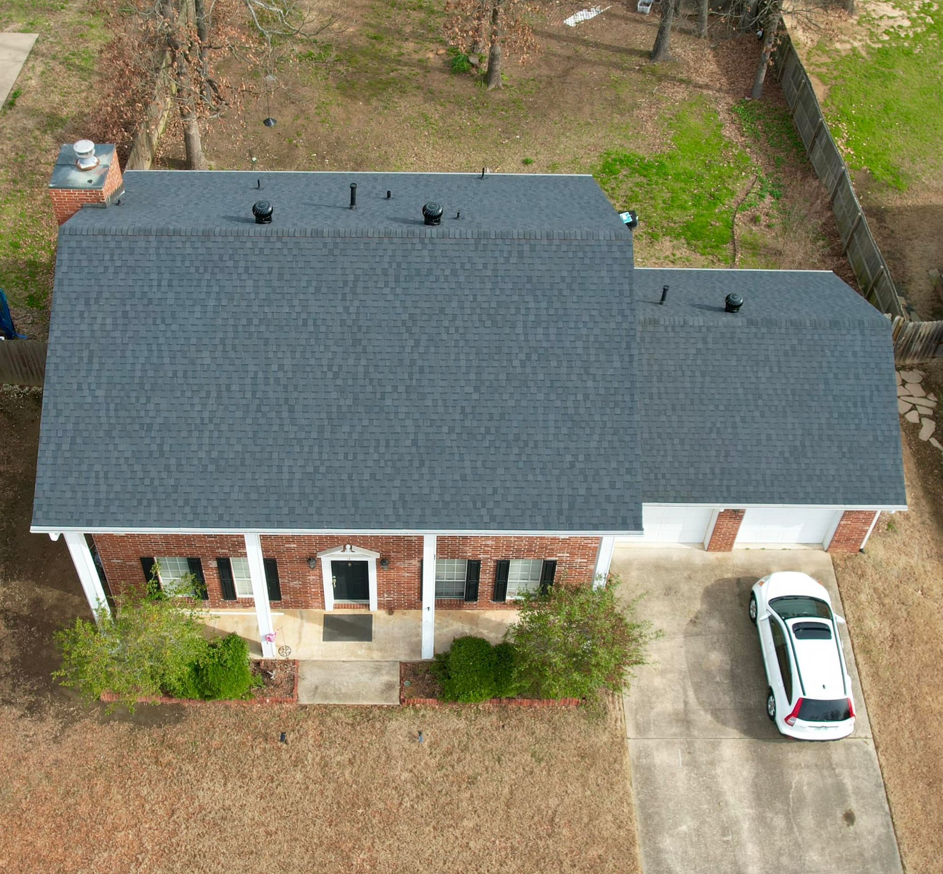Aerial view of a house with a gray roof and attached garage; white car parked in driveway.