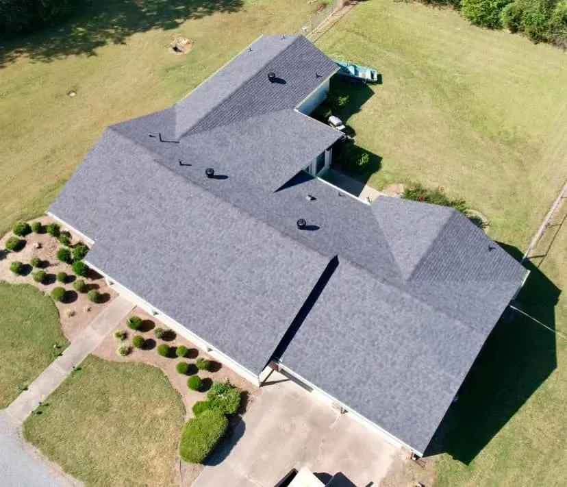 Aerial view of a gray-roofed house surrounded by green grass and a paved driveway.