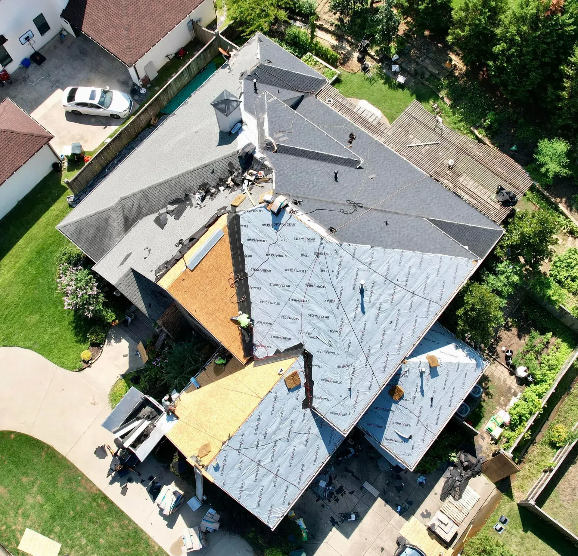 Overhead view of a house roof undergoing repair. Sections are missing shingles, revealing underlayment.