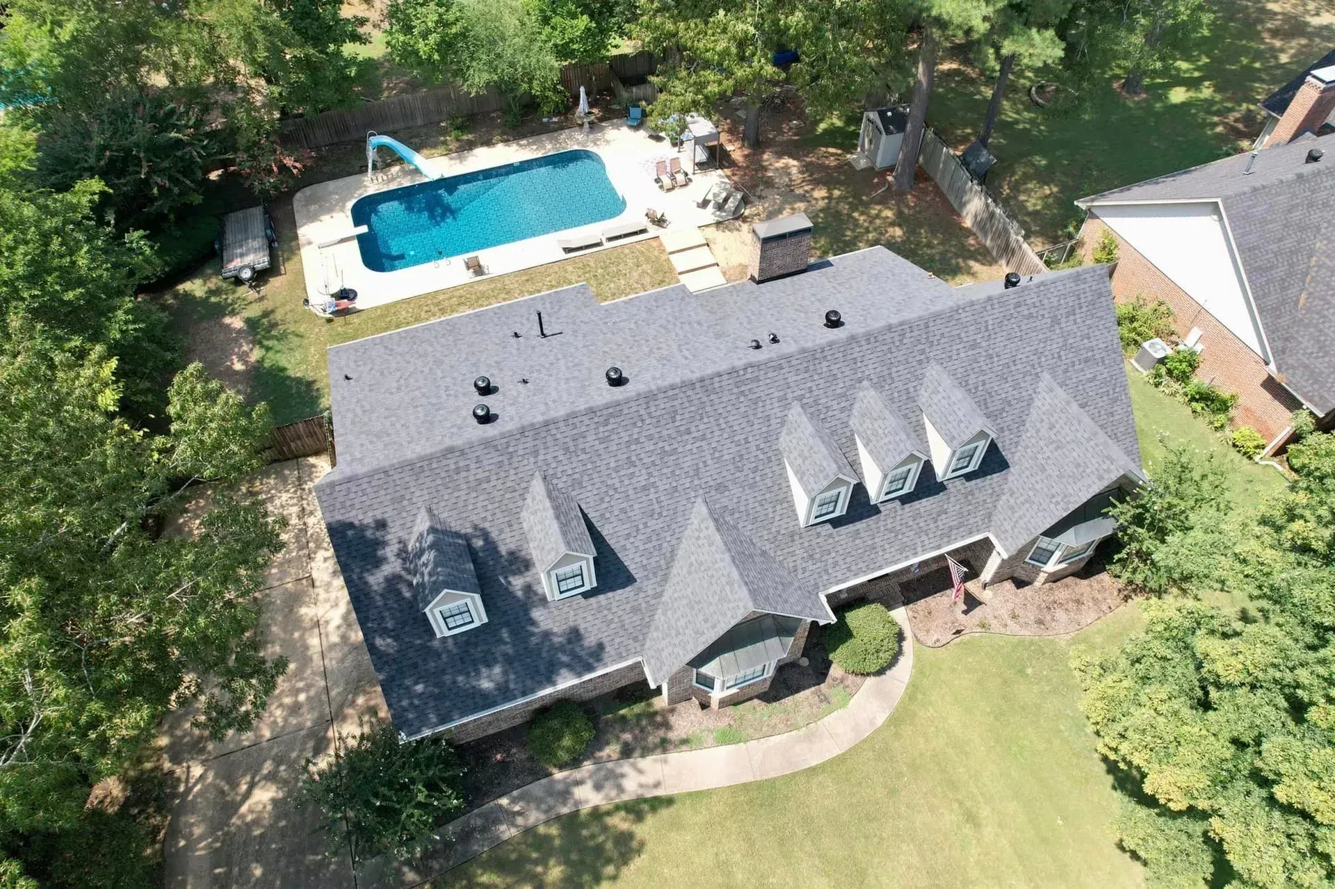 Aerial view of house with dark roof, three dormers, and a swimming pool in the yard.