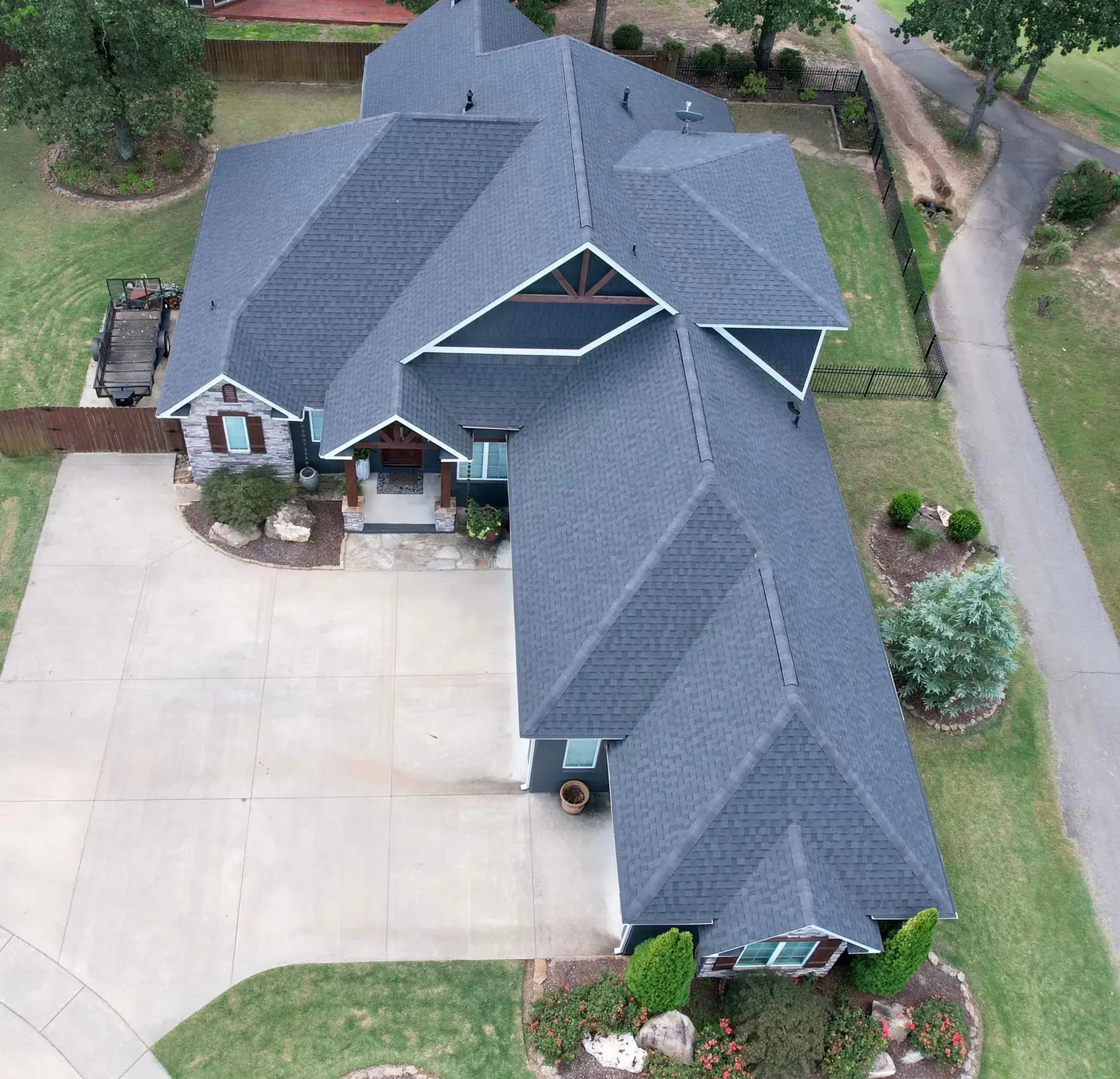 Aerial view of a dark gray roofed house with a long driveway surrounded by green grass.