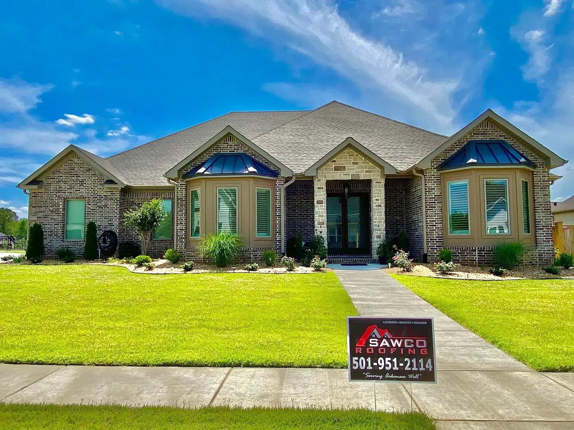 House with brick exterior, green lawn, blue sky. A for sale sign in front.