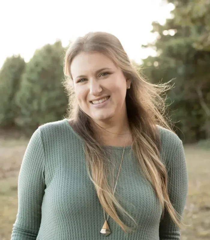 A woman wearing a green sweater and a necklace is smiling for the camera.